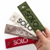 A hand displays three colorful tags marked "solo," connected by a woven keychain.