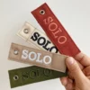 A person holds four colorful tags labeled "solo," attached to a woven keychain.