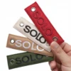 A person holds four colorful leather tags attached to a woven keychain, showcasing a variety of textures and hues.