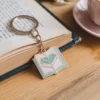 كتاب مزيّن بسلسلة مفاتيح لعشاق الكتب، موضوع بجانب فنجان قهوة دافئ.