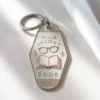 Ein Schlüsselanhänger mit einer Brille und einem aufgeschlagenen Buch als Symbol für die Liebe zum Lesen und zu buchbezogenen Themen.