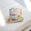 Эмалевая булавка с изображением книги и кофе, символизирующая любовь к чтению и уютным моментам.
