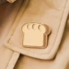 A gold enamel pin shaped like a slice of bread, perfect for adding a whimsical touch to any outfit.