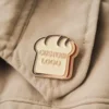 A gold pin featuring a stylized bread logo, representing a theme of baking or food-related interests.