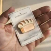 A hand holding a small enamel pin shaped like a loaf of bread, showcasing a cute and whimsical design.