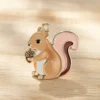 Pequeño colgante en forma de ardilla sobre un fondo rosa y marrón, que resalta su adorable diseño y artesanía.