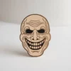 Una spilla che mostra un volto sorridente, combinando un'espressione spensierata con elementi della cultura horror.