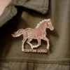 Une épingle portant le logo d'un cheval est attachée à une veste en jean, ce qui en fait un accessoire élégant sur le thème de l'équitation.