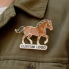 Individu portant une veste ornée d'un logo de cheval et d'un pin's de cheval, affichant un look décontracté mais élégant.