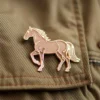 Un pin's sur le thème du cheval, placé sur une veste, avec un fond marron qui en rehausse l'aspect.
