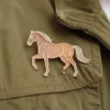 Un pin's de cheval marron sur une veste, mettant en valeur le style équestre.