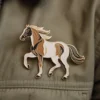Une épingle à cheval marron et blanc attachée à une veste en jean, présentant un motif équin détaillé.