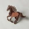 Épingle en émail représentant un cheval marron sur fond blanc, mettant en valeur son design détaillé et ses couleurs vives.