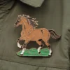 Une veste verte ornée d'une épingle à cheval décorative, soulignant l'amour des chevaux.