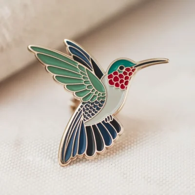 A colorful hummingbird enamel pin displayed on a clean white surface, showcasing intricate details and vibrant colors.