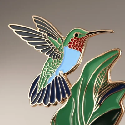 Enamel pin of a hummingbird set against a lush green and blue background, highlighting its delicate features and colors