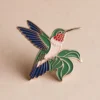 Un colorido alfiler esmaltado de un colibrí, con llamativos tonos verdes y rojos, perfecto para los amantes de las aves.