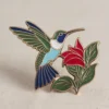 Broche de esmalte con un colibrí y una flor, un accesorio encantador para quienes aprecian las joyas únicas con temática de la naturaleza.