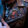 Un hombre sostiene una chaqueta de cuero adornada con varios pins de punk rock, haciendo gala de un vibrante despliegue de estilo personal.