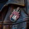 Chaqueta de cuero negro con un diseño de una guitarra roja y un pin punk rock pegado a ella.