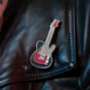 Primer plano de una insignia de guitarra roja sobre una chaqueta de cuero negro, que representa la moda punk rock.