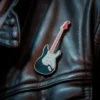 Un pin negro de guitarra punk rock atado a una chaqueta de cuero, mostrando un estilo atrevido y vanguardista.