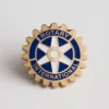 Pin de Rotary International colocado sobre una superficie blanca, símbolo de la afiliación al Club Rotario.