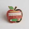 An apple pin inscribed with "Outstanding Teacher," representing recognition and gratitude for exceptional educators.