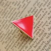 閉じた本の上に置かれた「トライアングル・ルージュ」と書かれた赤い三角形のピン。