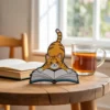 A cat perched on a book next to a cup of tea, featuring a cute cat bookmark sticking out from the pages.