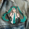 Individual with blue hair and green eyes, sporting a hat adorned with a Miku pin.