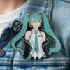 A person with blue hair wearing a hat and a green tie, featuring a Miku pin on their hat.