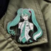 A pin featuring a girl in a green dress, inspired by Miku, with vibrant colors and a playful design.