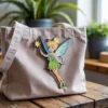 A tote bag featuring Tinkerbell, adorned with a colorful enamel pin of the fairy.