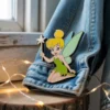 Tinker Bell enamel pin attached to a denim jacket, showcasing her iconic pose and vibrant colors.