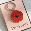 Red enamel poppy keychain displayed on a card, showcasing its vibrant color and design.