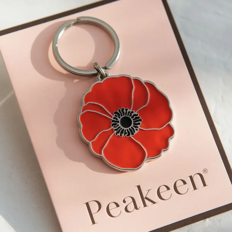 Red enamel poppy keychain displayed on a card, showcasing its vibrant color and design.