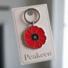 Red enamel poppy keychain with a black and white tag, symbolizing remembrance and honoring veterans.