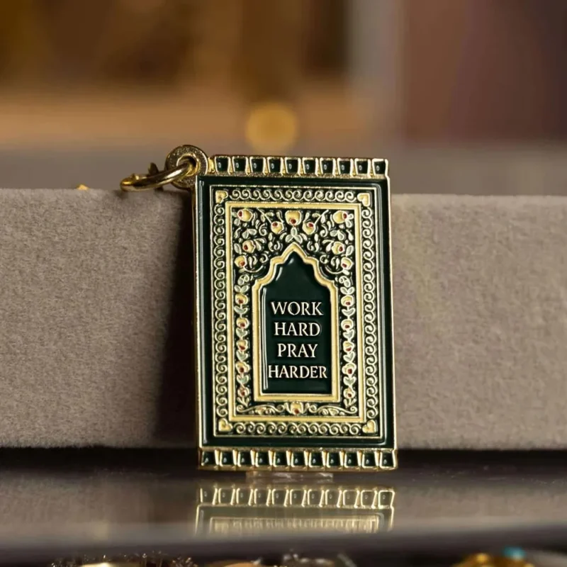 A gold and black book with a gold chain, designed as a prayer mat keychain.