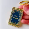 Close-up of a hand gripping a prayer mat keychain inscribed with "stay humble," symbolizing a reminder for humility.