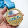 A person proudly holds a gold enamel swimming medal inscribed with "metric challenge."