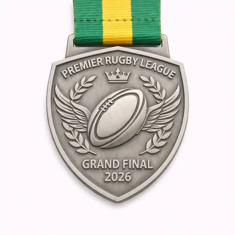 A silver Premier Rugby League Grand Final 2026 medal featuring a rugby ball with wings, laurel wreaths, and a crown, suspended from a green and yellow ribbon.