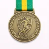 A gold Rugby Champions 2026 Finals medal featuring a running rugby player inside a shield, surrounded by laurel wreaths, with a green and yellow ribbon.