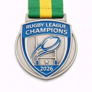 A silver and blue Rugby League Champions medal for 2026, featuring a stylized rugby ball flying through goalposts, a star beneath the posts, and a green and yellow ribbon attached at the top.
