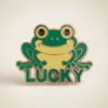 Enamel frog pin featuring the word "lucky" in a playful font, symbolizing good fortune and charm.