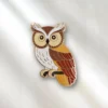 Enamel pin of a brown and white owl set against a white background, highlighting its intricate details and playful expression.