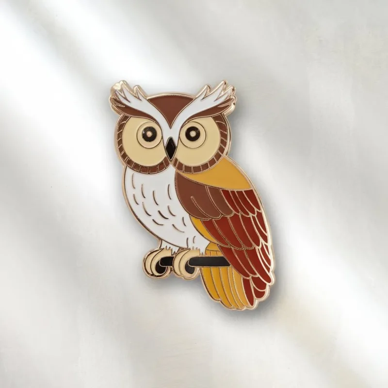 Enamel pin of a brown and white owl set against a white background, highlighting its intricate details and playful expression.