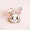 White rabbit enamel pin on a pink background, showcasing a cute and whimsical design perfect for collectors.