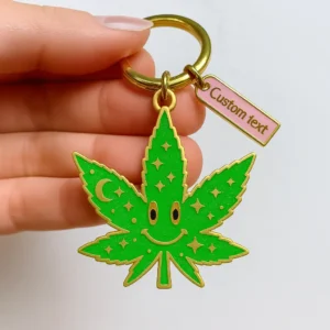 A green marijuana leaf keychain featuring a cheerful smiley face design.