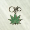 A marijuana leaf keychain featuring a green leaf design attached to a silver metal keyring.
